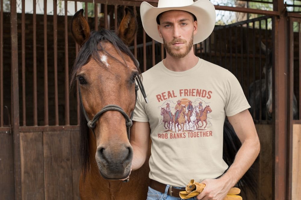 Cowboy wearing Frontier Rogue Real Friends Rob Banks Together graphic tee in barn with horse