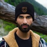 Man wearing Frontier Rogue black beanie with brown logo in forest setting