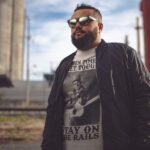 Man wearing Frontier Rogue When Times Get Tough Stay on the Rails graphic tee in outdoor railroad setting