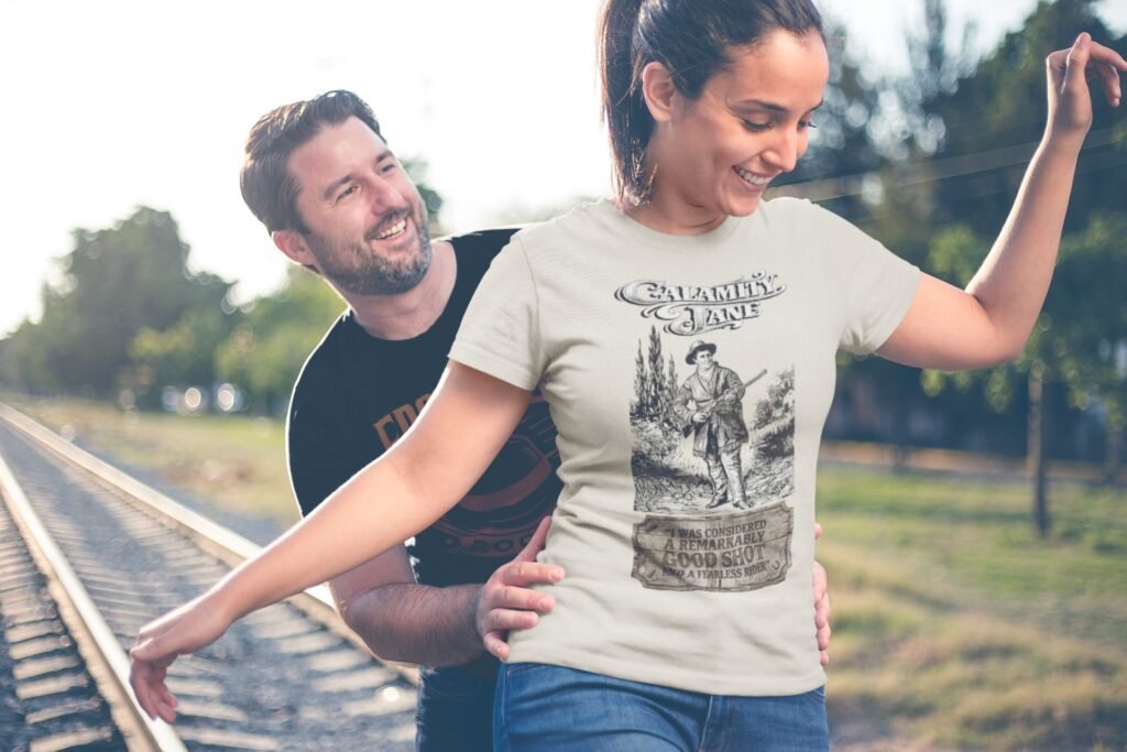 Woman wearing Frontier Rogue Calamity Jane shirt on train tracks with man